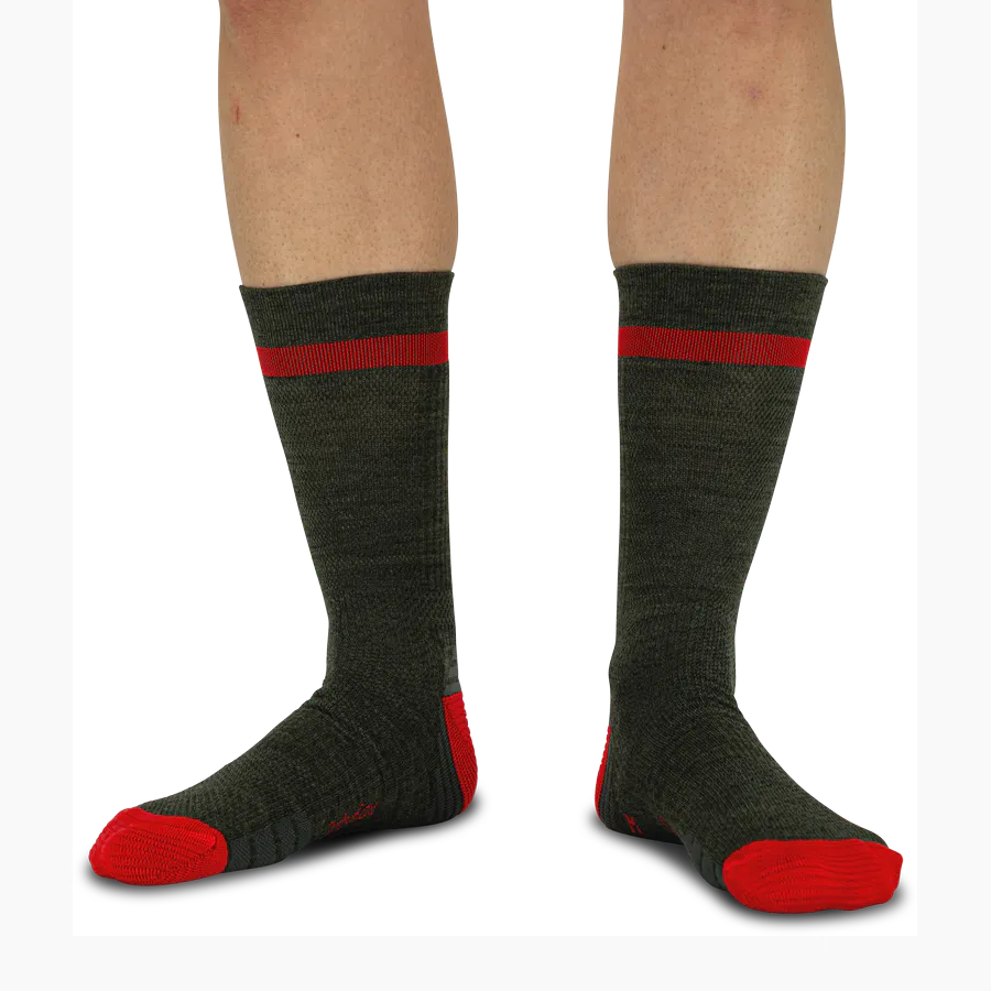 Dunkel graphitgraue Socken bis zur Wadenmitte. Breiter roter Streifen am Bund, rote Kontraste an Ferse und Zehen. Strukturierte Oberfläche der Heritage Socken wirkt robust; getragen an Unterschenkeln vor neutralem Hintergrund.