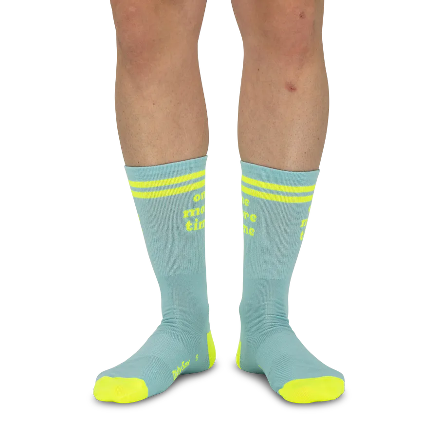 Des jambes sur fond blanc, portant des chaussettes bleu clair ornées de deux bandes jaune vif chacune au niveau du bord-côte. Sur le devant, l'inscription « one more time » en jaune. Les zones des orteils et du talon sont également de couleur jaune vif.