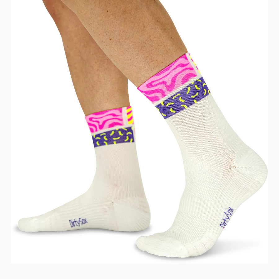White socks with colourful cuffs in a neon style. On the shaft: a wide neon pink stripe with a wave pattern, accompanied by a thin neon yellow band and a purple stripe featuring yellow shapes. A splash of colour for your feet.