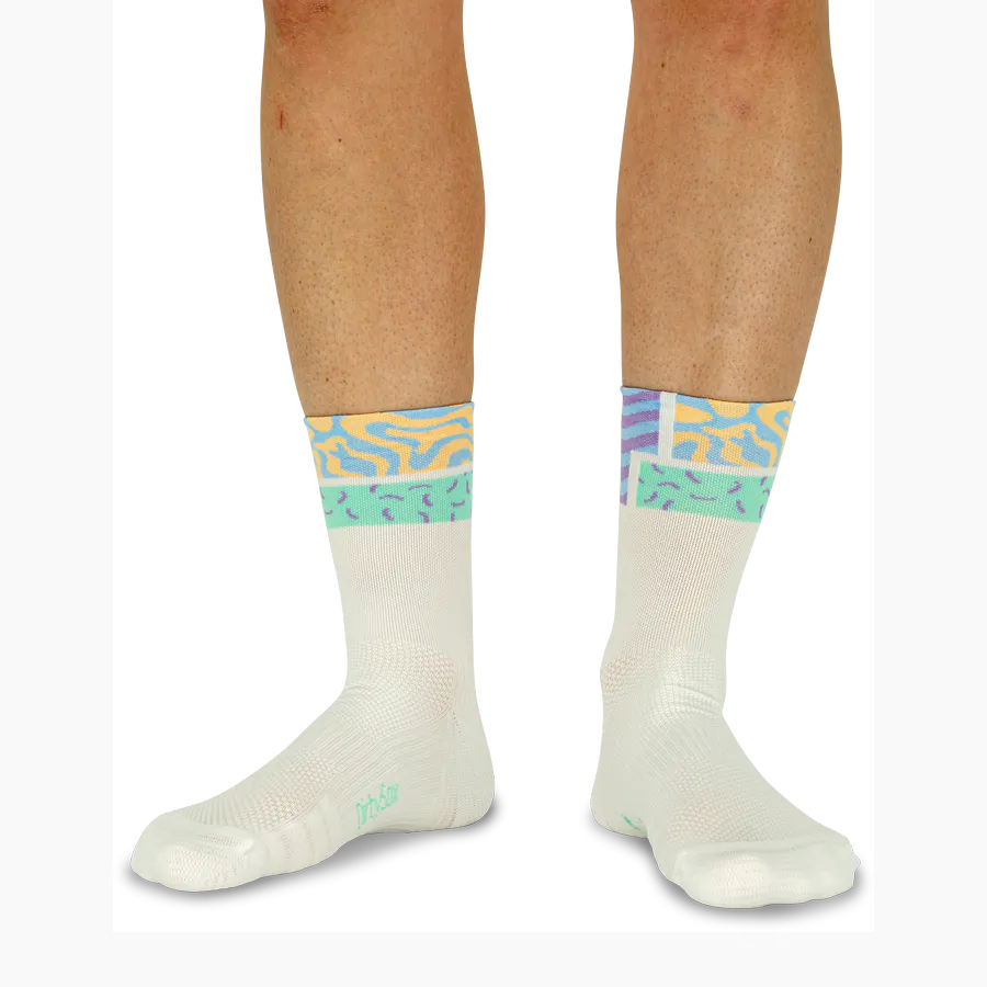 Two legs are wearing cream-coloured socks with a colourful, abstract pattern on the cuff. Wavy lines and irregular shapes in pastel shades such as light blue, yellow, mint green and lilac create a vibrant ‘Pastel Flow’ design.