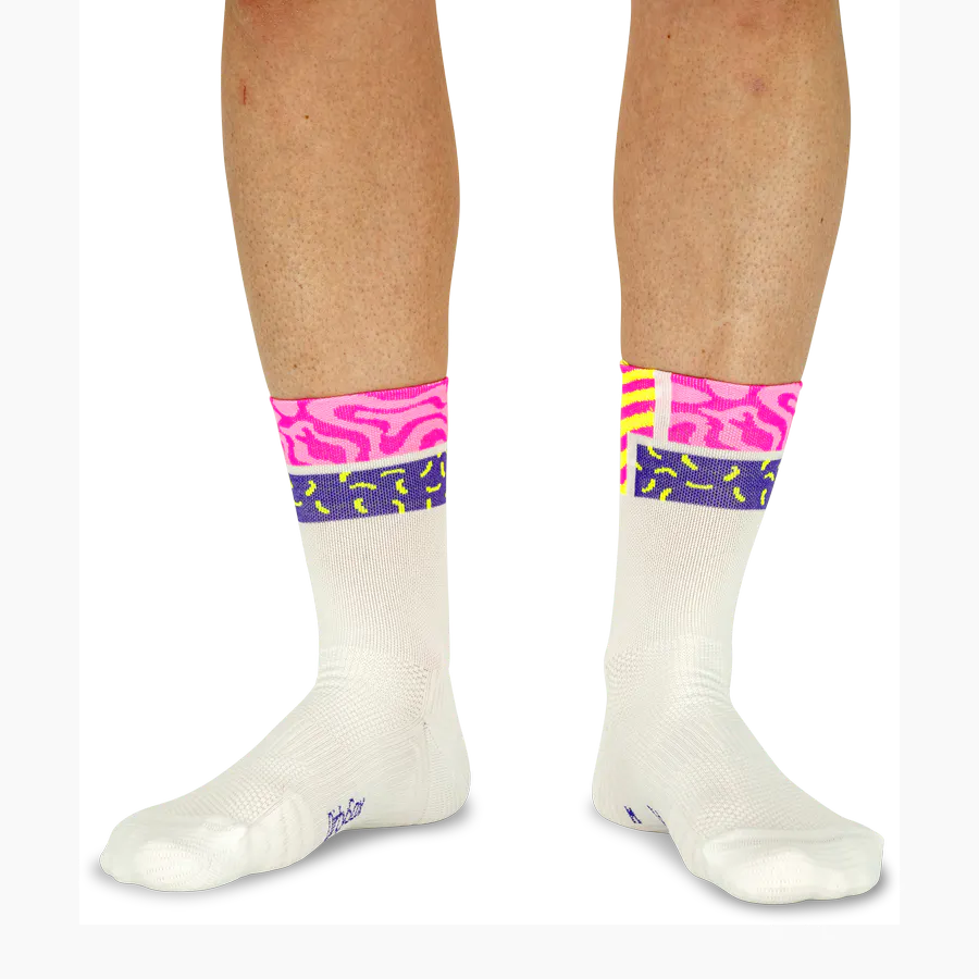 Two legs are wearing white socks with colourful cuffs in the ‘Neon Vibe’ design. The top section is bright pink with organic patterns, followed by a bright yellow stripe with purple ‘Color Pop’ accents, and finished off with dark purple.