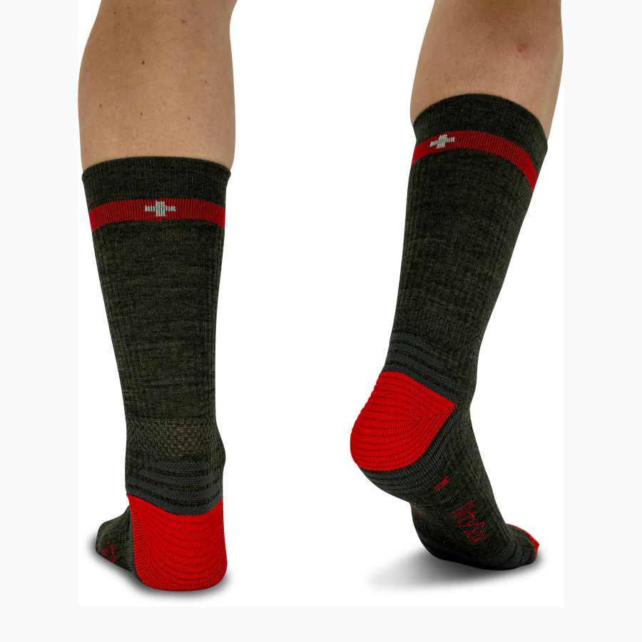 Dark grey socks in the ‘Graphite Shadow’ colourway with striking red accents on the cuffs, heel and toes. A red stripe adorns the leg, alongside a white cross referencing Alpine Heritage. The socks feature a ribbed texture and are set up.