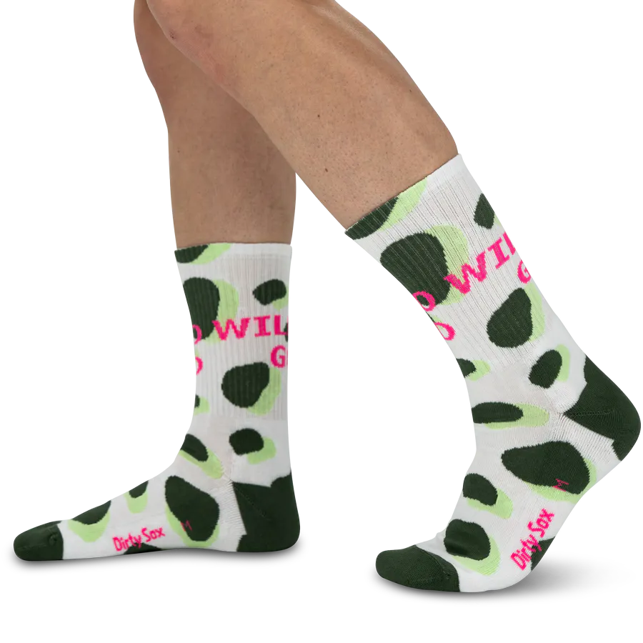 Chaussettes blanches avec motif animalier de taches irrégulières vert foncé et vert clair, rappelant une girafe. Inscription « GO WILD » rose vif sur le côté. Orteils et talon contrastés en vert foncé.