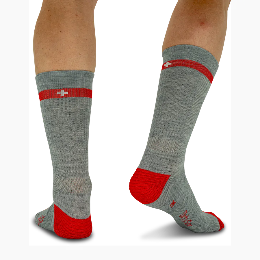 Grey merino wool trekking socks with a red heel and toe section. A red stripe featuring the white Swiss cross runs along the leg. The ‘ DirtySox ’ logo is embroidered in red on the side. Sturdy knitted fabric designed for outdoor use.
